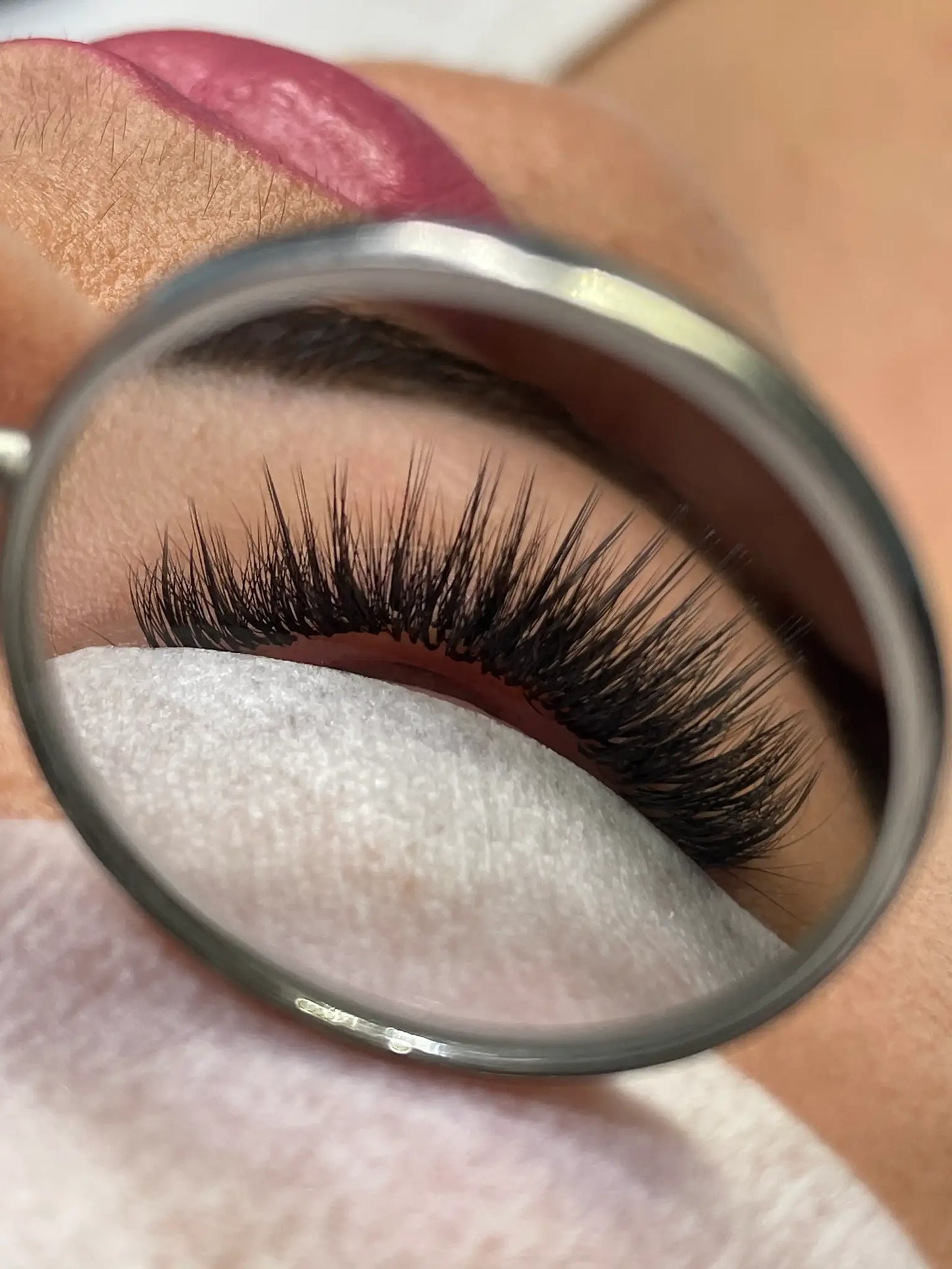 Close-up view through lash mirror showing a wispy lash set with dramatic spikes, styled in the Kim K lash effect.