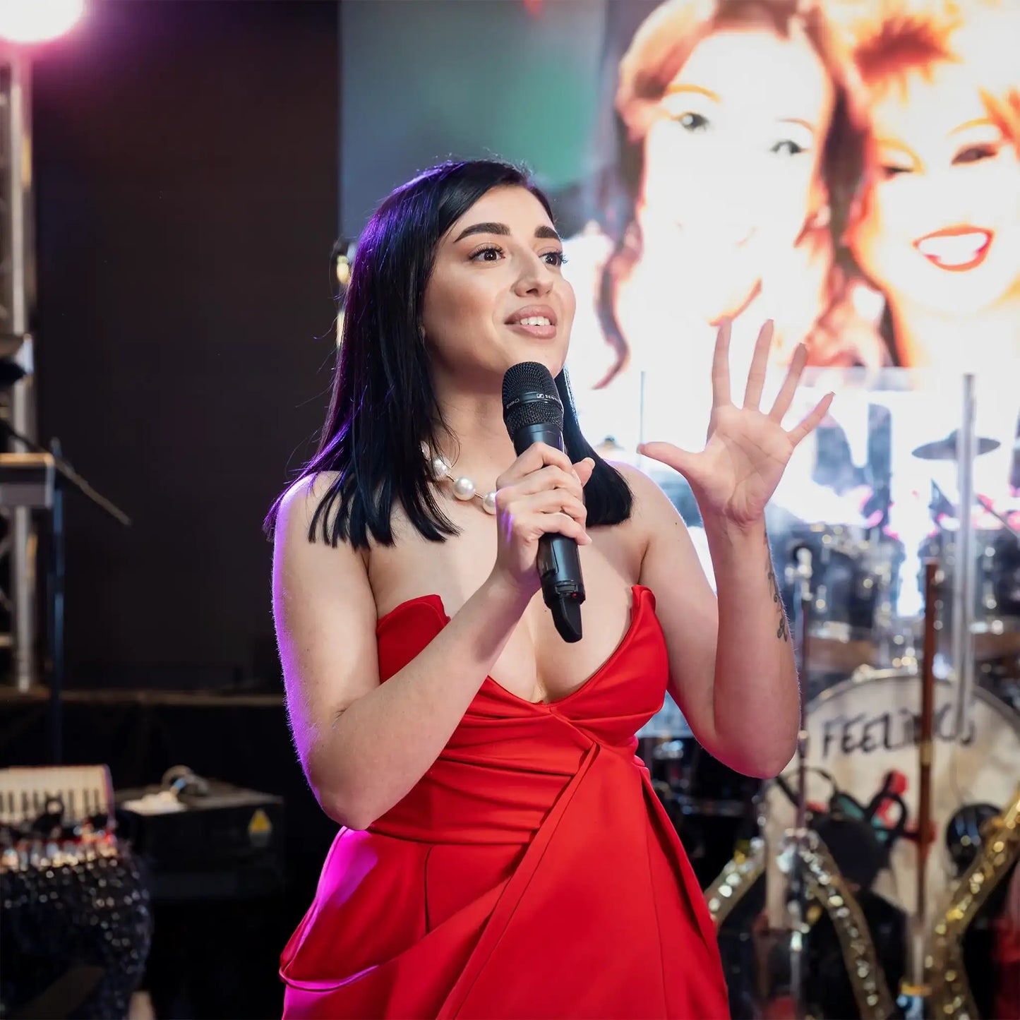 Loredana Irimia delivering a speech on stage at a lash industry event, wearing a red dress and holding a microphone.