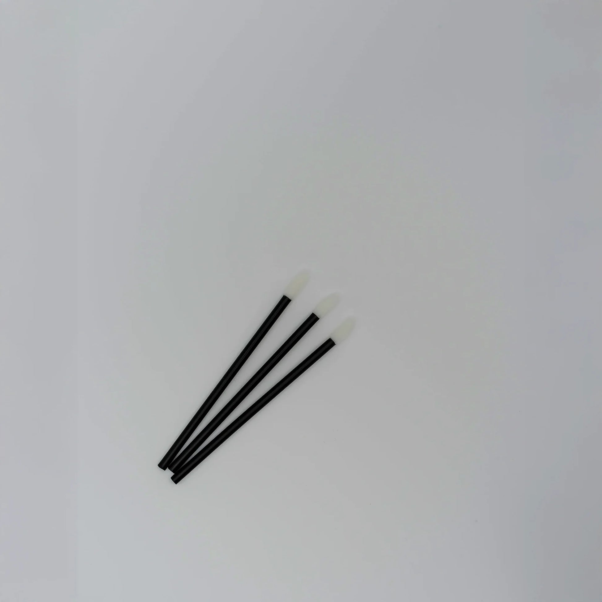 Close-up of disposable lip gloss applicators for eyelash extensions, black wand with soft white tip, essential tool for lash pre-treatment, The Lash Box Shop.