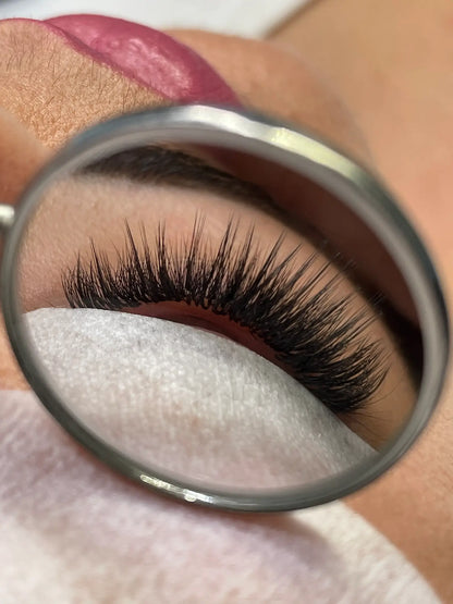 Close-up view through lash mirror showing a wispy lash set with dramatic spikes, styled in the Kim K lash effect.